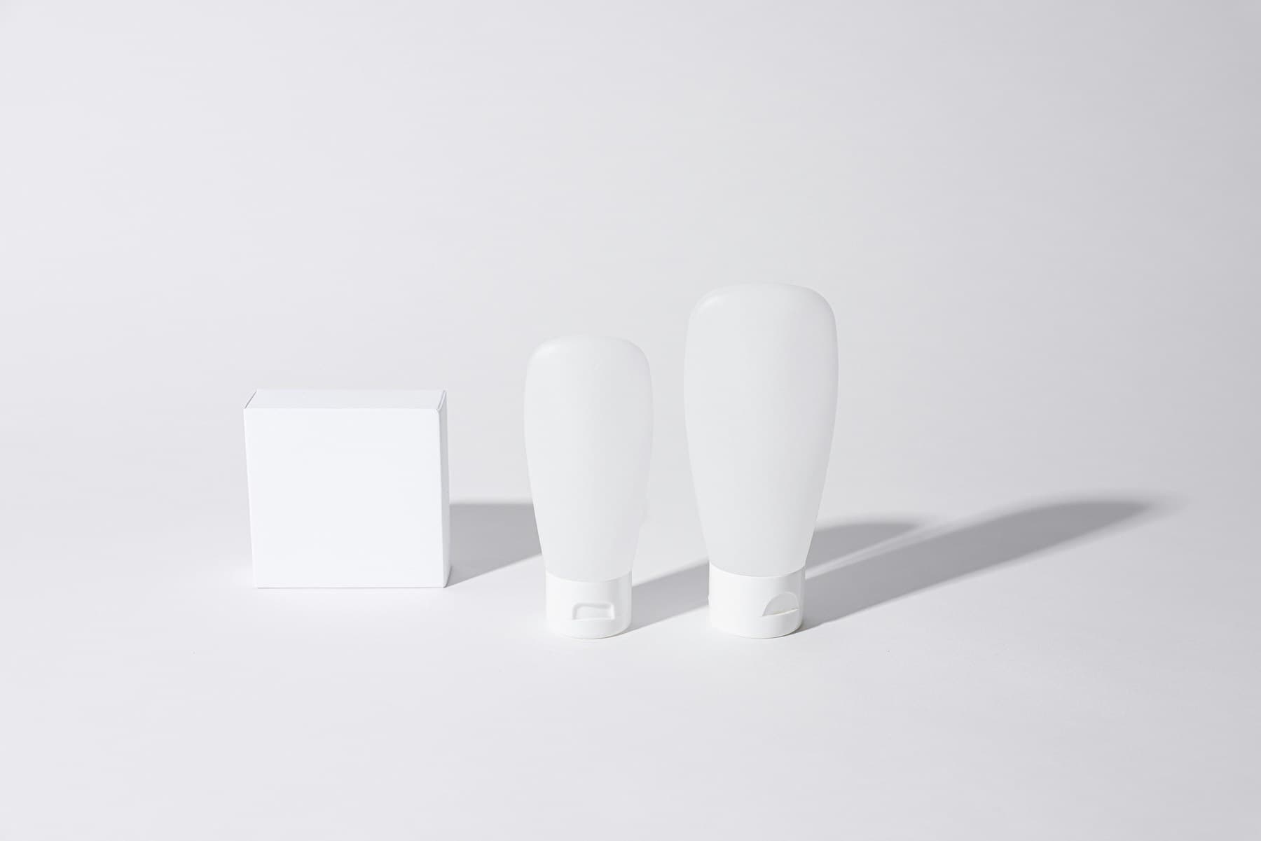 Minimal white skincare tubes and carton with directional shadows